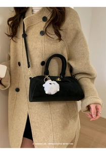 Dettaglio borsa Boston in camoscio nero con ciondolo peluche su cappotto color cammello