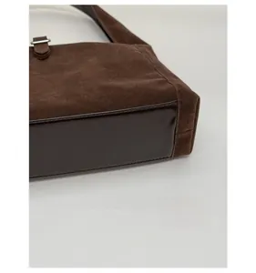 Detailed close-up of dark brown suede shoulder bag with reinforced shiny leather base