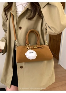 Dettaglio borsa Boston in pelle caramello con chiusura dorata e ciondolo di peluche bianco