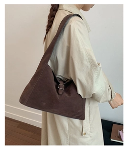 Detail of dark brown suede crescent shoulder bag with square metal buckle on female model