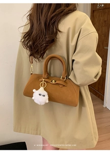 Dettaglio della borsa in ecopelle marrone con chiusura dorata e ciondolo a pompon bianco