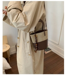 Chic two-tone bucket bag with wooden bead charm worn with a classic beige trench coat