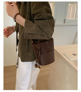 Detail of contrast-textured bucket bag showing suede stitching and beaded tassel charm