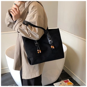 Dettaglio della borsa tote nera con nappine di perline decorative e finitura opaca