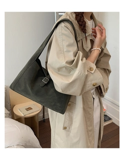 Detail of dark green suede tote bag with silver buckle worn on model's shoulder