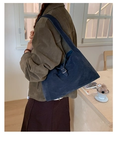 Detail view of deep blue suede shoulder bag with silver buckle on model in cafe setting