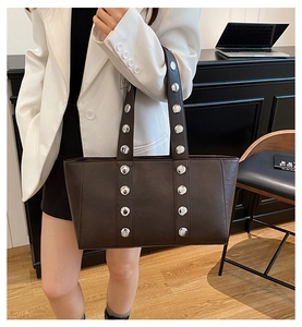 Brown leather tote bag featuring parallel silver rivet details shown in an office setting