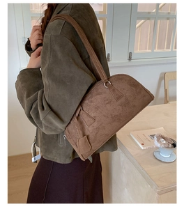 Detail of a brown suede bowling bag shown on a model in a warm lifestyle setting