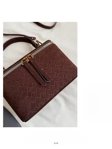 Detail of dark brown woven suede handbag with golden double zippers and soft texture