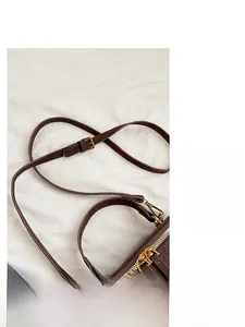 Detail of adjustable slim brown leather shoulder strap and gold hardware on retro crossbody bag