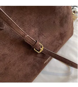 Close-up of brown suede bucket bag featuring adjustable strap with gold buckle and logo