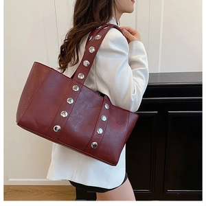 Detail of burgundy leather tote bag with oversized silver studs worn over a white blazer