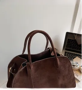 Detail of dark brown suede bucket bag featuring golden hardware and adjustable side straps