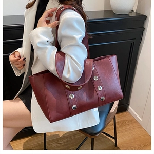 Detail of burgundy leather tote featuring silver eyelet studs and smooth wide strap