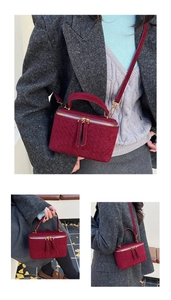 Close-up of a burgundy vanity case bag with woven texture and gold metal hardware detail