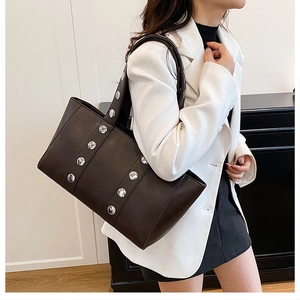 Détail d'un grand sac cabas marron foncé avec clous argentés porté par un mannequin