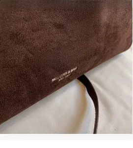 Detail of gold-stamped logo and textured brown suede leather on large bucket bag