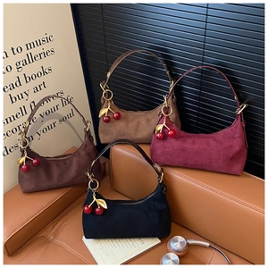 Detailed view of suede tote bags in four colors with cherry charms on a leather sofa