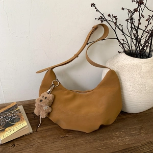 Close-up of caramel suede crescent shoulder bag with a cute plush teddy charm on wood