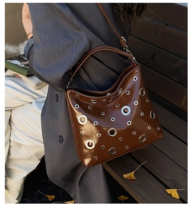 Détail du sac hobo marron brillant avec œillets argentés dans un décor de parc automnal