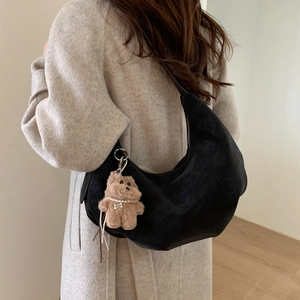 Detail of black suede hobo bag with cute dog charm worn over a beige wool coat