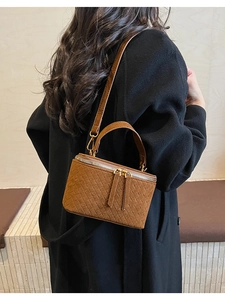Rear view of a model wearing a brown woven box bag with adjustable chain strap detail