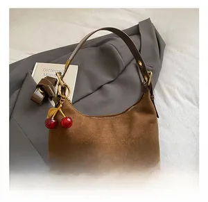 Detail of brown suede tote bag featuring a cute red cherry charm and golden hardware