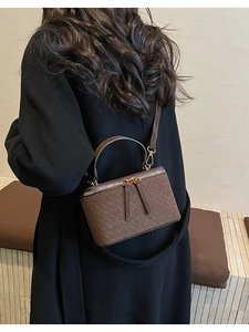 Mini brown woven box bag worn crossbody over a black coat with adjustable strap