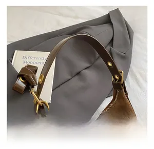 Detail of suede tote bag showing brown leather handle, metal buckle and cherry accessory
