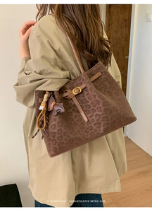 Detail view of leopard print tote bag with bear charm and leather strap on a model shoulder