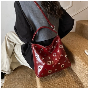 Détail du sac à main bordeaux brillant avec oeillets métalliques porté par le mannequin