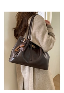 Detail of coffee brown leather tote bag with a bear charm on beige coat background