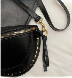 Detail of smooth gold zipper and fringe pull on a black studded crossbody bag