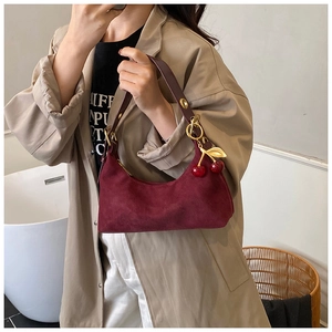 Detail of burgundy suede underarm bag with a decorative cherry pendant and gold buckle