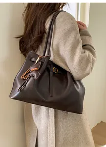Detail view of large dark brown leather tote bag with side buckle and bear charm