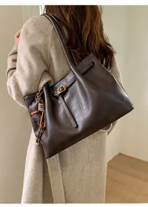 Detail of dark brown tote bag with bear charm on model in beige coat for autumn style