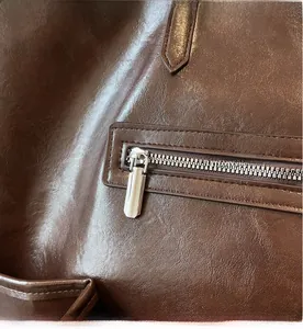 Détail de poche à fermeture éclair argentée sur un grand sac cabas en cuir marron