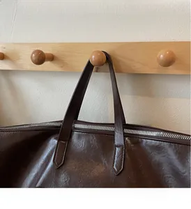 Détails des poignées renforcées et de la fermeture éclair argentée sur le sac en cuir brun