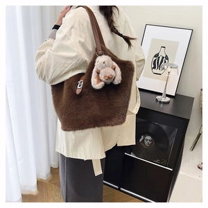 Detail of plush brown tote bag featuring leather strap and cute rabbit charm accessory