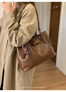 Close-up of a brown retro faux leather tote bag with a golden buckle and bear charm