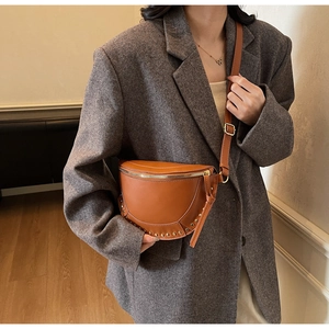 Close-up of brown half-moon crossbody bag with gold rivet detailing on a model