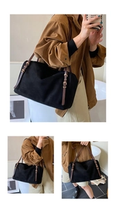 Close-up of black suede tote bag featuring brown leather straps and gold metal buckles