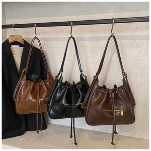 Three quilted drawstring bucket backpacks in caramel, black, and dark brown with metal hardware