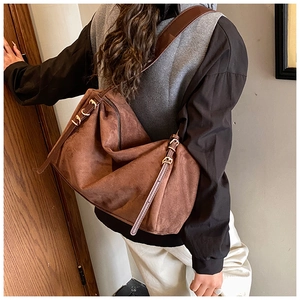 Detailed side view of large brown suede shoulder bag with gold metal buckle and zipper