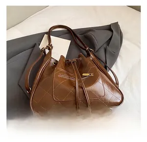 Detail of dark brown quilted faux leather bucket bag with gold zipper and drawstring