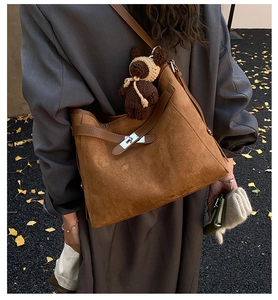 Detail of brown suede shoulder bag with cute bear charm and silver lock in autumn setting