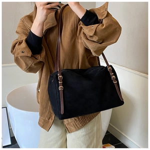 Detail of black suede tote bag featuring brown leather straps and gold buckle accents