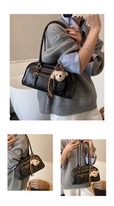Detail of a black leather underarm bag featuring dual straps and a plush puppy pendant