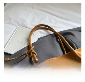 Brown tote bag detail featuring white contrast stitching and unique knotted handle detail