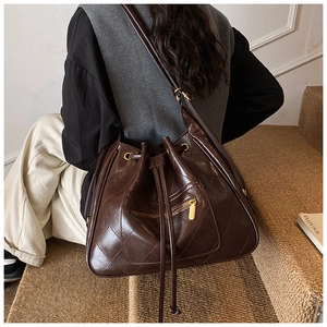 Detail of dark brown quilted bucket backpack with gold zipper and drawstring closure
